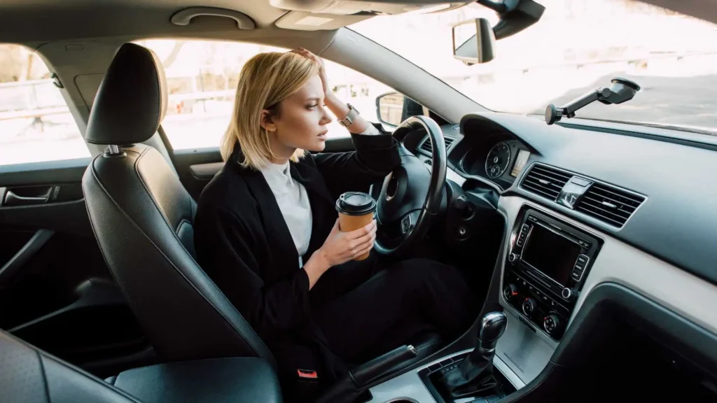 Stressed woman driver holding coffee cup in car, illustrating cost for driving record in Alabama